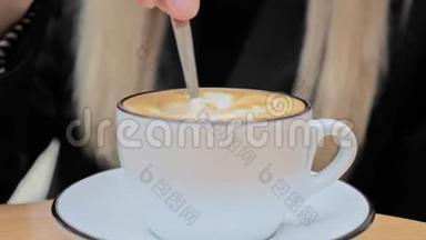 <strong>一个</strong>未被认出的白人金发女人用<strong>一个</strong>小<strong>勺子</strong>在一杯卡布奇诺咖啡中搅拌糖。